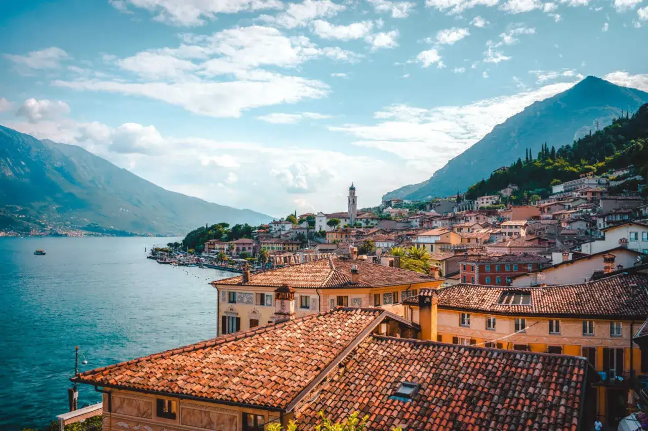 Malownicze miasteczko nad jeziorem Garda, z widokiem na góry i turkusową wodę. W oddali widać wieżę kościelną.