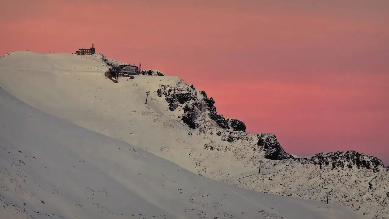 Zach&oacute;d słońca nad Kasprowym Wierchem. Czy szlak na Kasprowy Wierch jest trudny? Widok na ośnieżone szczyty i wyciągi narciarskie.