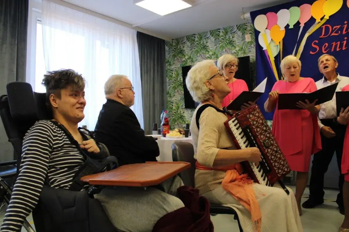 Wesoły występ z okazji Dnia Seniora: akordeonistka i chór śpiewają dla zgromadzonych.