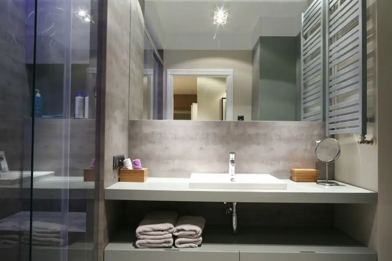 Nowoczesna łazienka z prostokątną umywalką na nodze, szarymi płytkami i podświetlaną kabiną prysznicową.