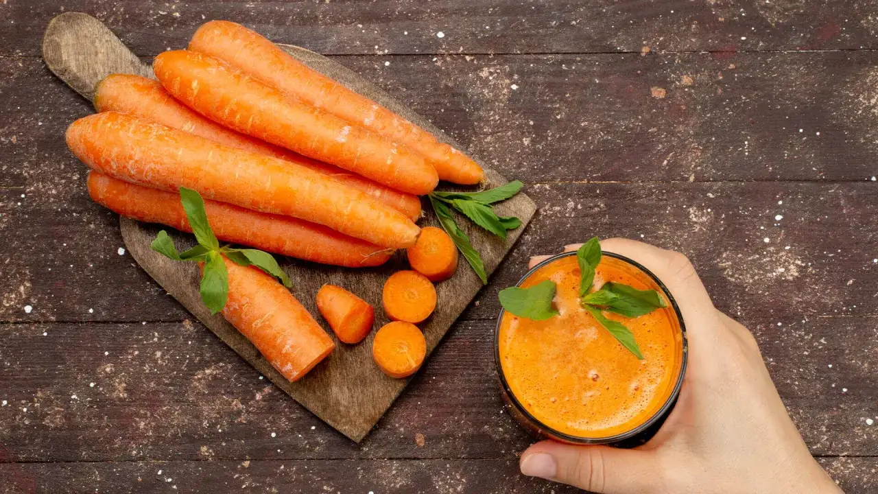Świeże marchewki na desce i szklanka soku. Czy gotowana marchewka traci witaminy? Zobacz, jak zachować ich najwięcej.