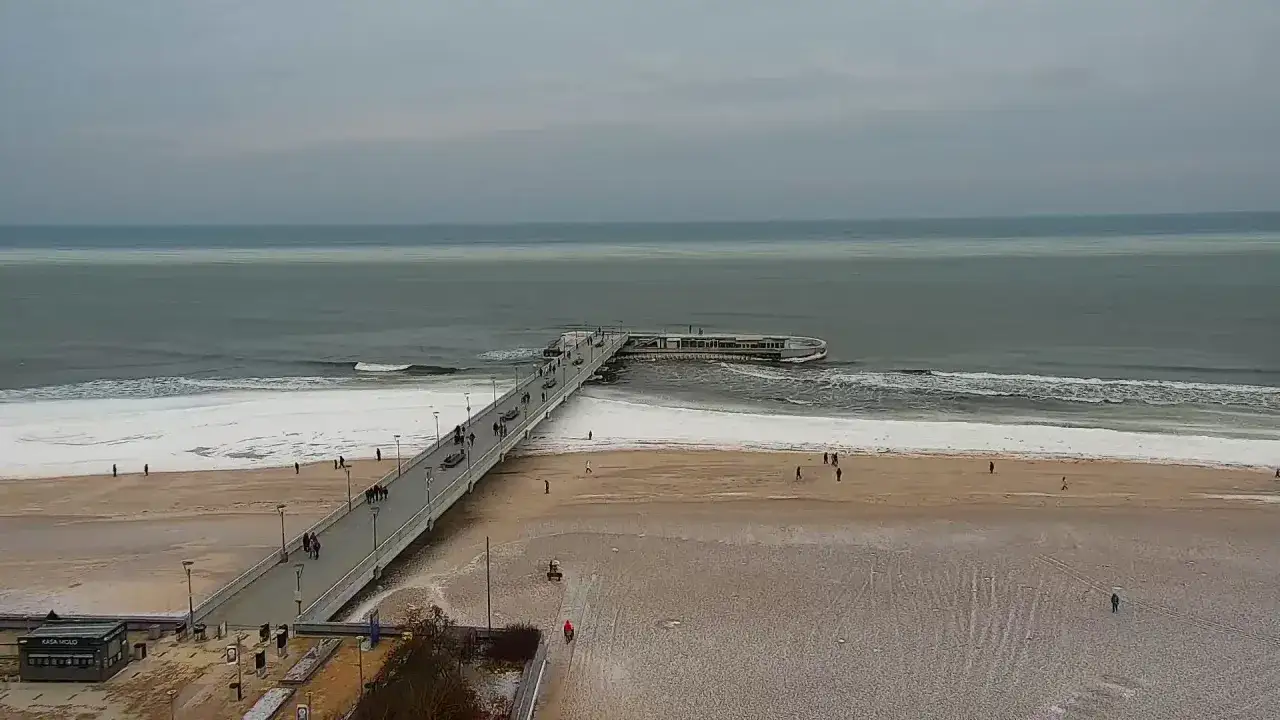 Spacerem po deptaku w Kołobrzegu, widać morze i plażę pokrytą śniegiem.