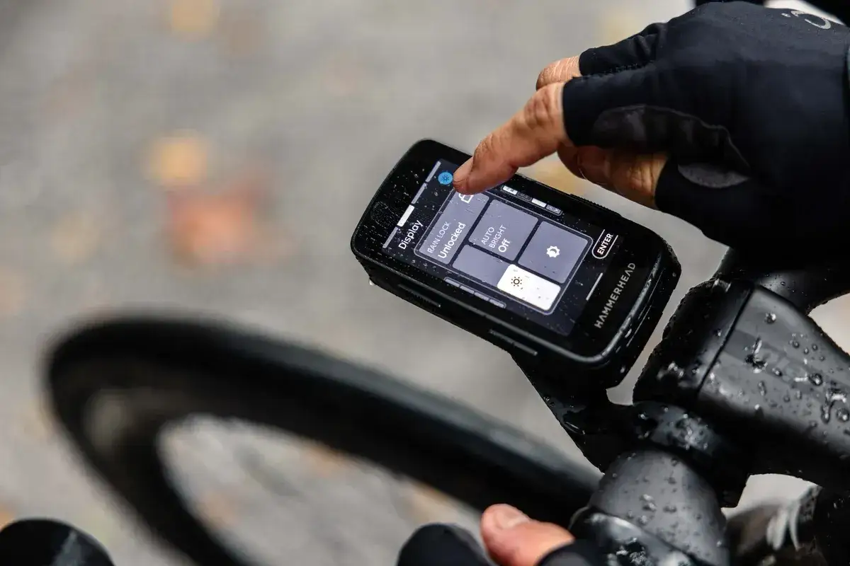 Rowerzysta dotyka ekranu Hammerhead Karoo 3, ustawiając opcje wyświetlacza podczas jazdy w deszczu.