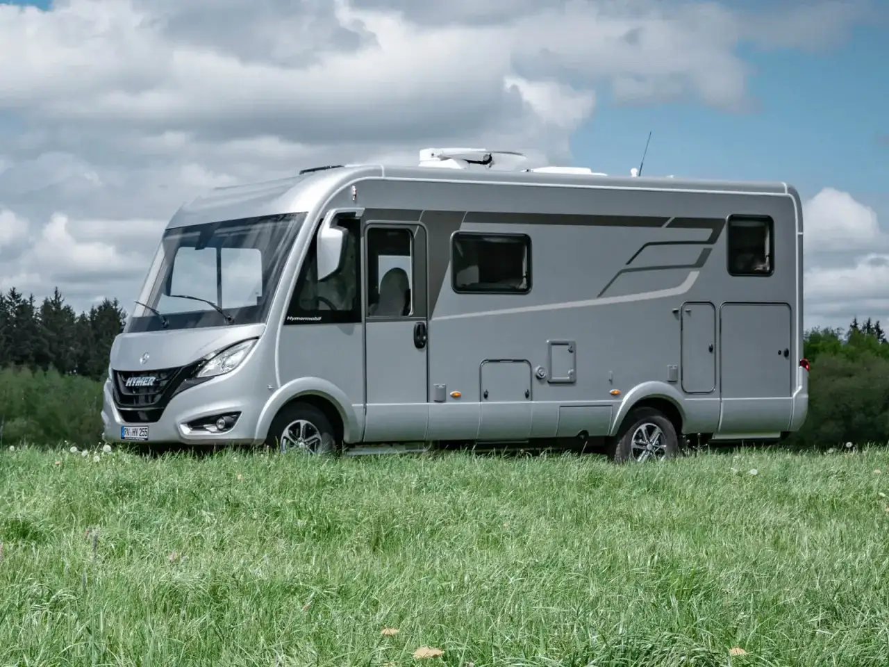 Srebrny kamper Hymer, produkt Erwin Hymer Group, stoi na zielonej łące.
