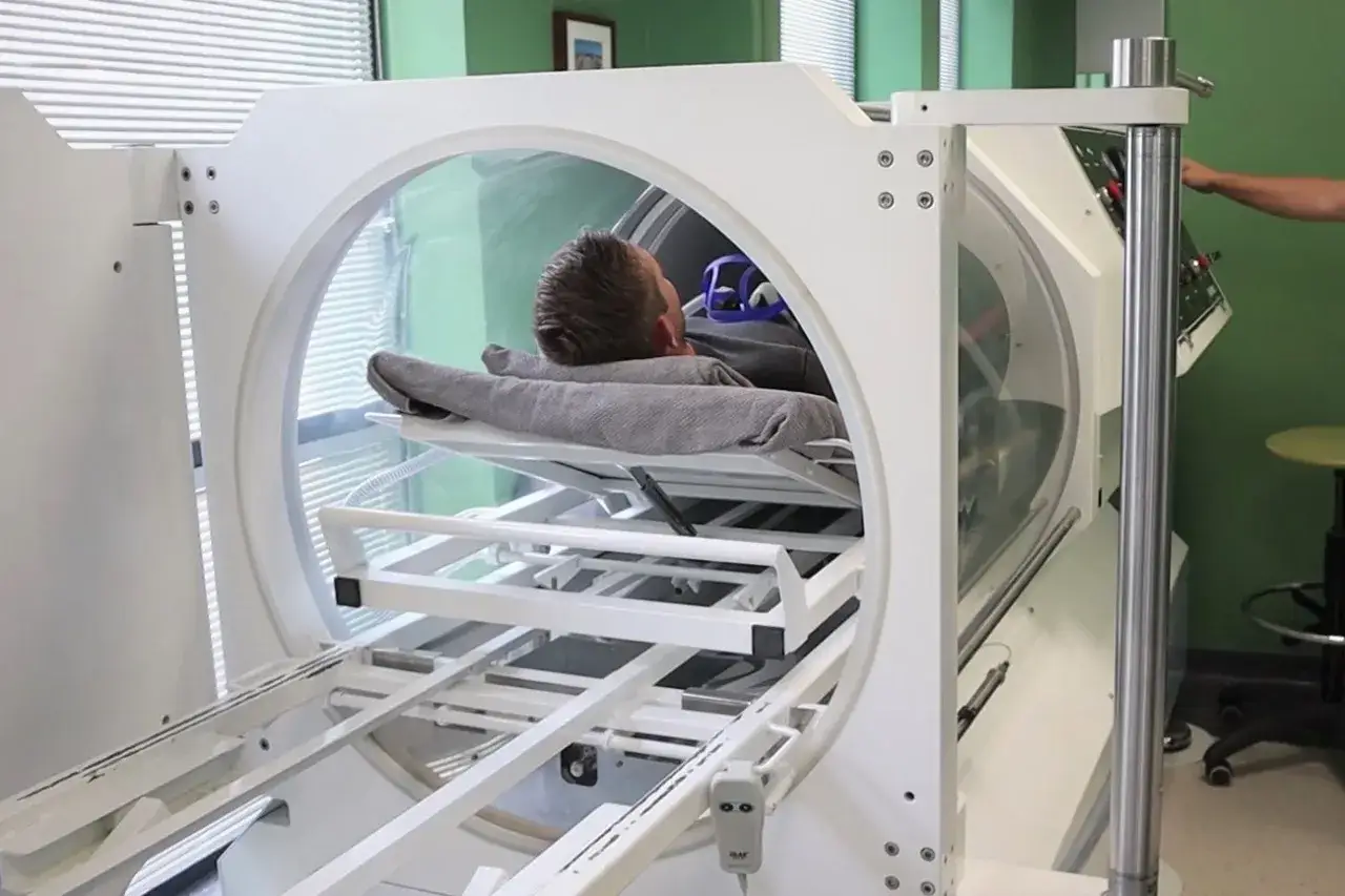 Mężczyzna leży w komorze dekompresyjnej, która jest używana do terapii tlenowej. Pozwala to zrozumieć, jak działa komora dekompresyjna.