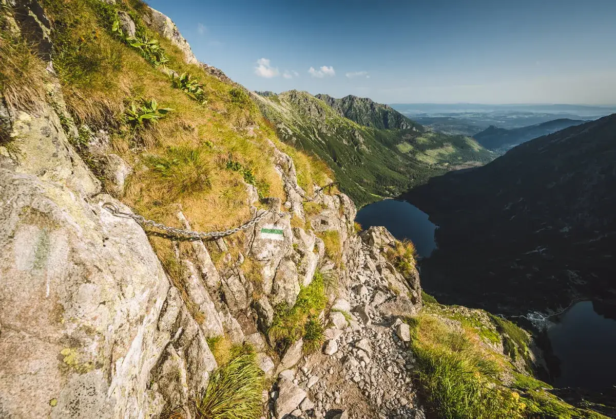 Szlak turystyczny z łańcuchami prowadzi przez skaliste zbocze w kierunku przełęczy pod Chłopkiem. Widok na jezioro i góry.