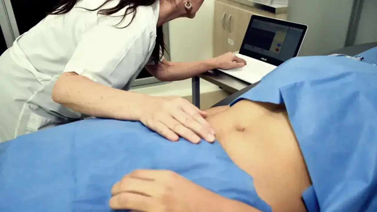 Lekarz bada brzuch pacjentki, sprawdzając, czy można prowadzić ciążę na NFZ i prywatnie. Na ekranie laptopa widoczne są dane medyczne.