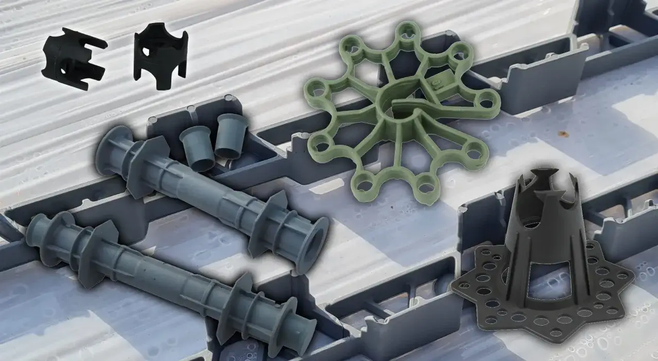 Różnorodne dystanse do betonu: gwiazdki, tuby i stożki, ułożone na szarej siatce.