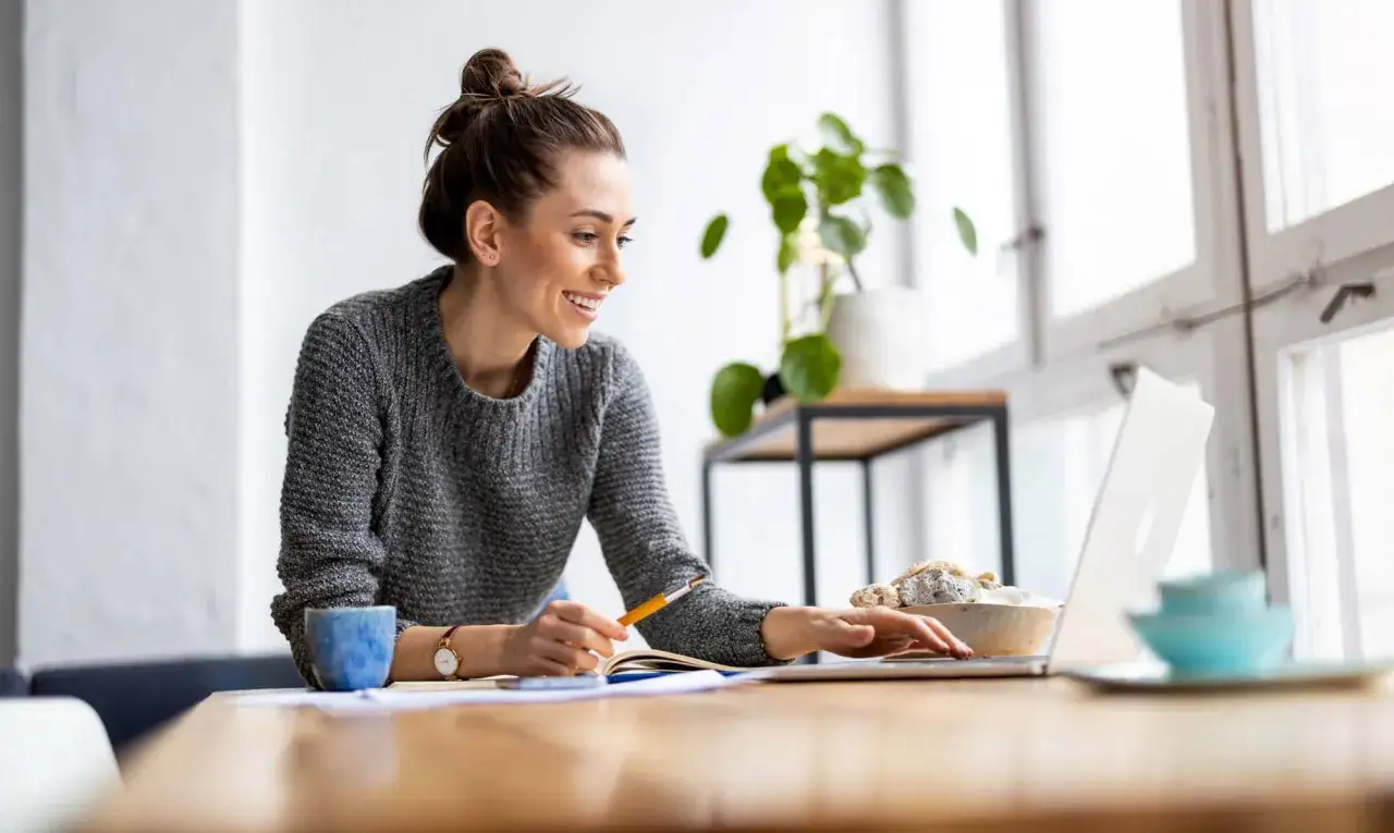 Uśmiechnięta kobieta pracuje przy laptopie, szukając informacji o kredyt na dowód bez umowy o pracę.