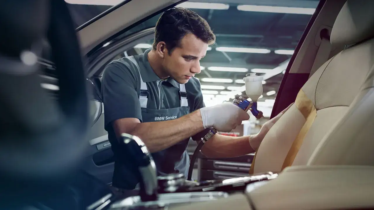 Profesjonalny detailer samochodowy BMW Service odnawia tapicerkę fotela, używając specjalistycznego sprzętu.