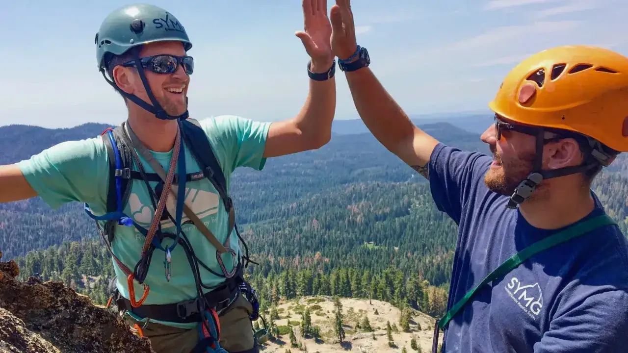 Dwóch wspinaczy w kaskach świętuje sukces na szczycie góry. Różne rodzaje wspinaczki to ich pasja.