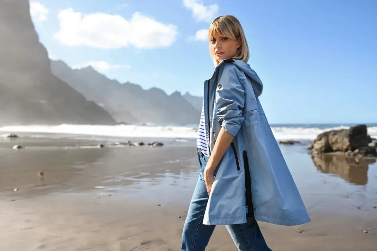 Stylowa kobieta w lekkiej kurtce i jeansach spaceruje po plaży. Idealny przykład, jak się ubrać nad morze, gdy pogoda jest zmienna.