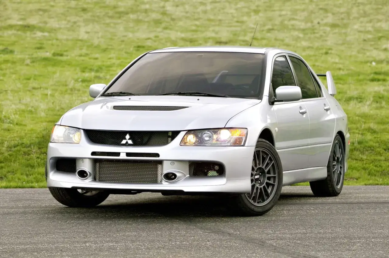 Srebrny Mitsubishi Lancer Evo 11 z charakterystycznym wlotem powietrza i spojlerem, gotowy do jazdy po zielonym polu.