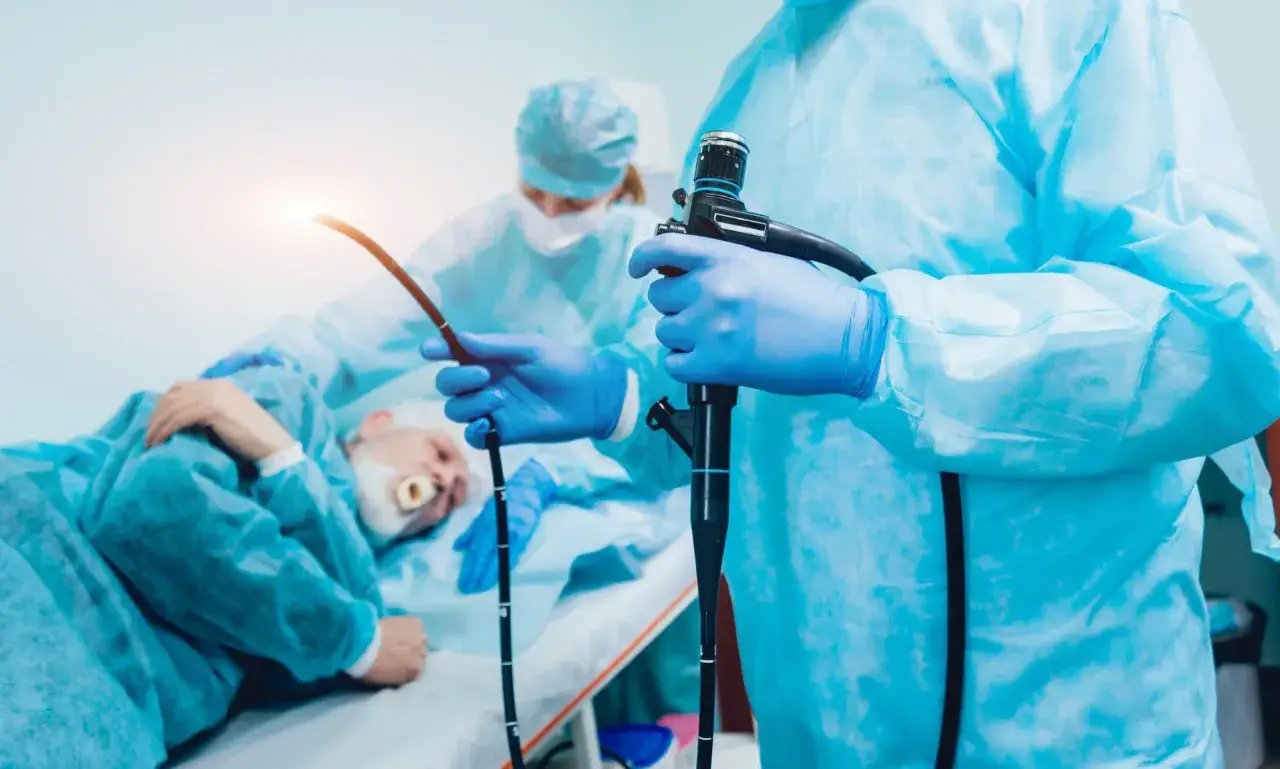 Lekarz w niebieskich rękawiczkach trzyma endoskop. Pacjent leży na stole. Czy przed gastroskopią można brać leki? Zapytaj lekarza.