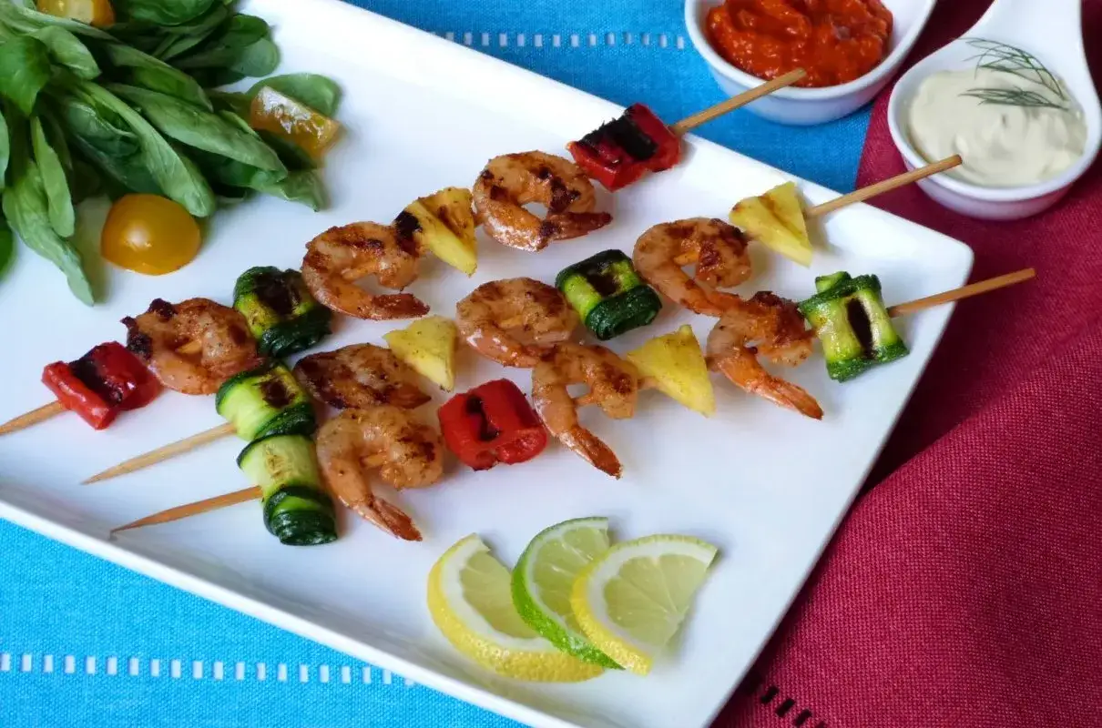 Krewetki z grilla z papryką, cukinią i ananasem na białym talerzu, podane z cytryną i limonką.
