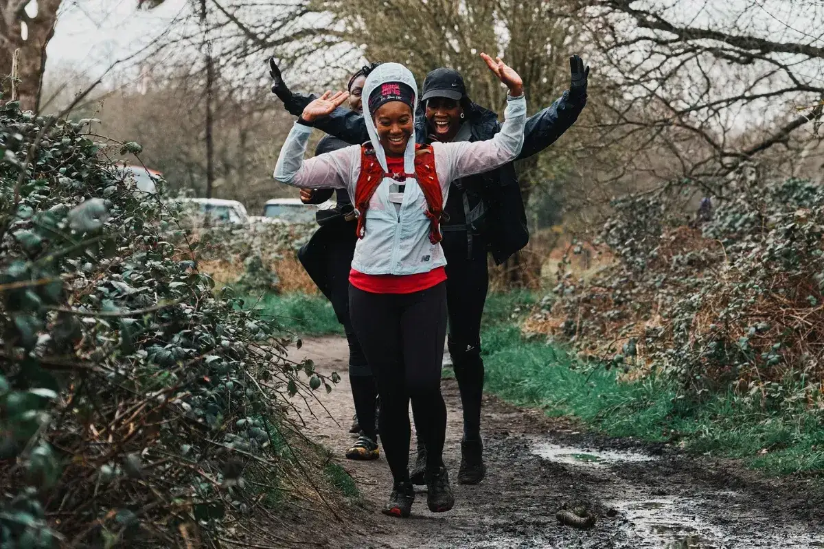 Trzy kobiety radośnie biegną w mrozie po błotnistej ścieżce, machając rękami.