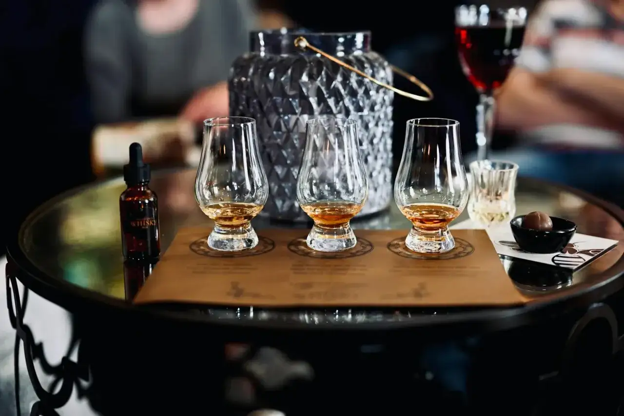 Degustacja whisky: trzy kieliszki z bursztynowym trunkiem, buteleczka z pipetą i czekoladka. Idealne akcesoria, by dowiedzieć się, jak pić whisky.