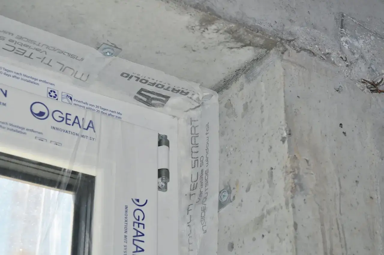 Szczegół zbliżenia na ciepły montaż okna. Folia paroizolacyjna MULTI-TEC SMART chroni połączenie okna z betonową ścianą.
