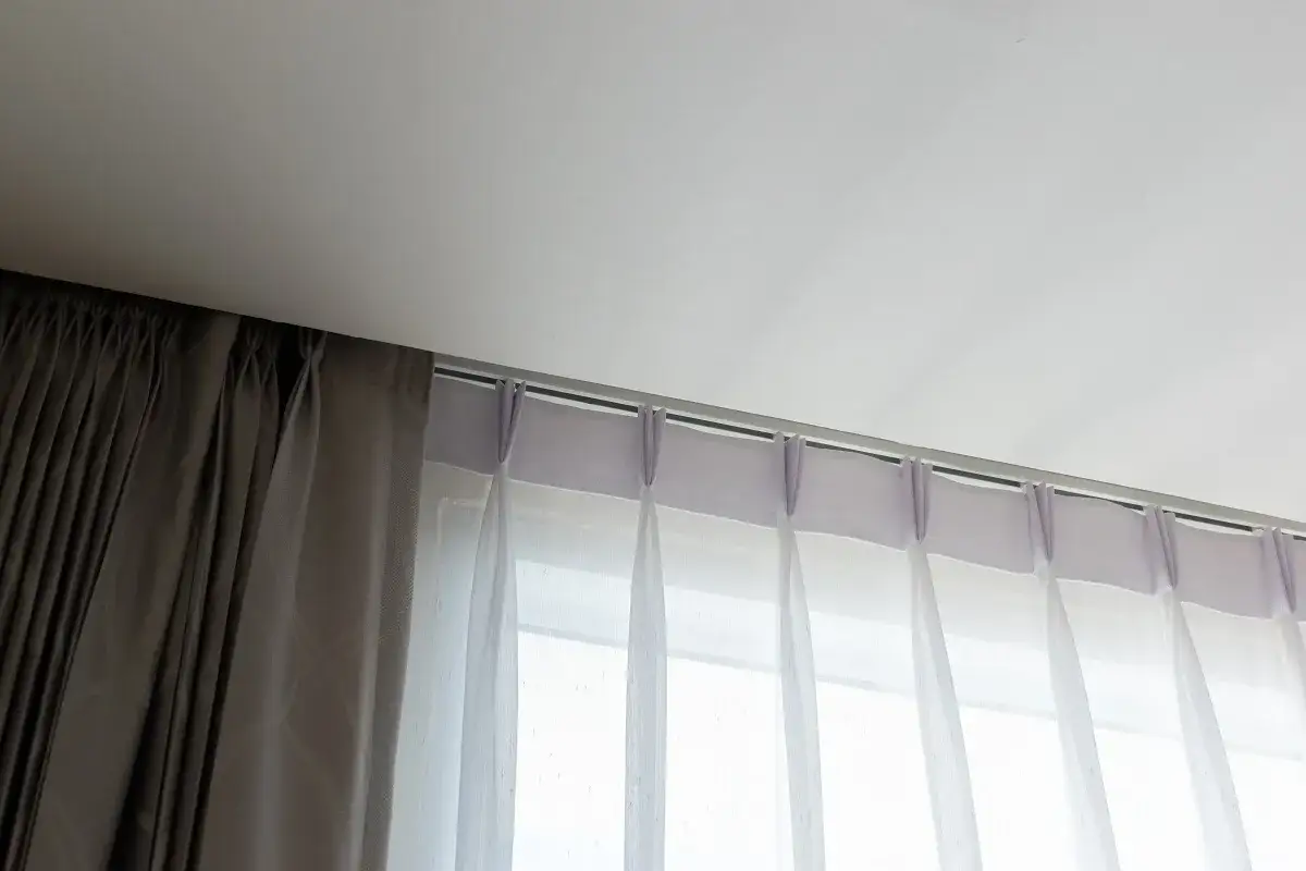Szyna sufitowa dwutorowa z zasłonami: ciemną i jasną, tworzącymi warstwy.