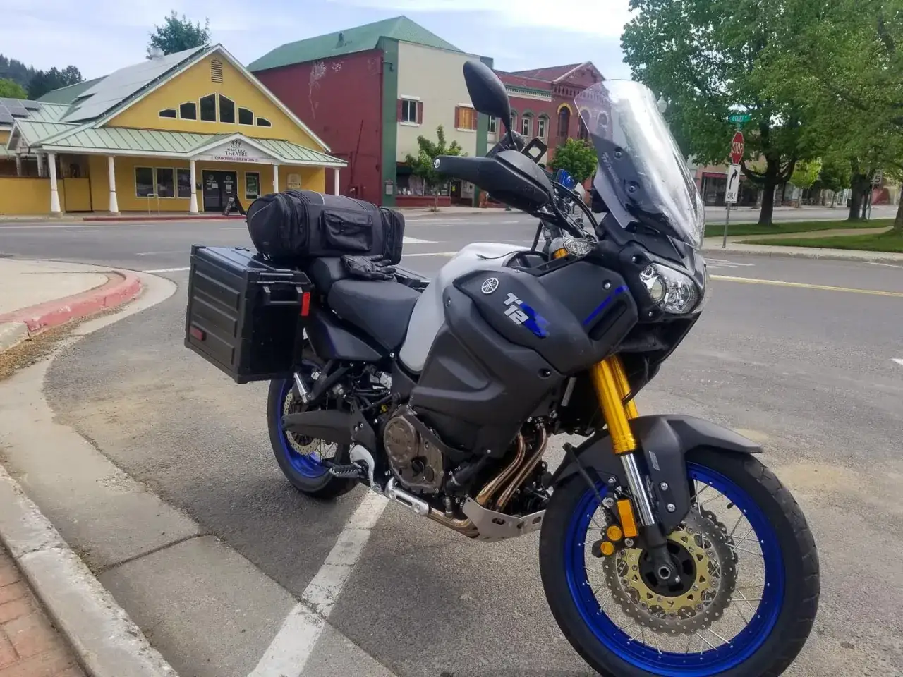 Gotowy na przygodę motocykl Yamaha Super Tenere 1200 z kuframi, zaparkowany przed żółtym budynkiem teatru.