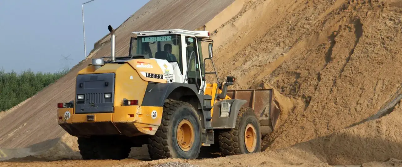 Ładowarka Liebherr pracuje na placu budowy, gdzie piasek jest ładowany. Warto wiedzieć, ile waży metr sześcienny kruszywa.