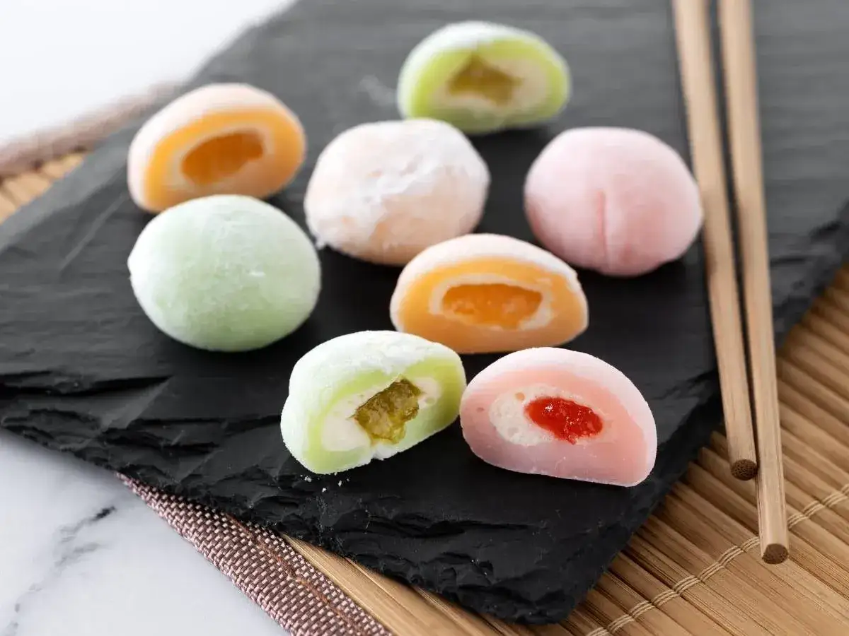 Kolorowe mochi z nadzieniem owocowym i kremowym, idealne do domowego przepisu. Patyczki do jedzenia obok.