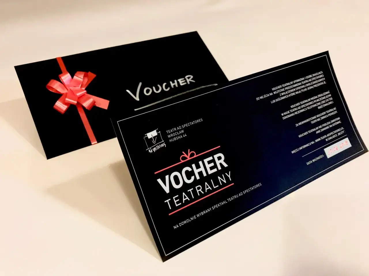 Idealny prezent urodzinowy: voucher do Teatru AD Spectatores na dowolny spektakl. Czerwona wstążka dodaje mu uroku.
