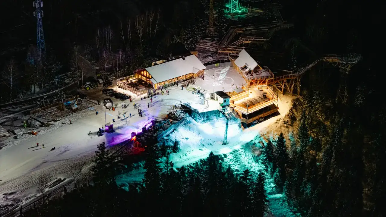 Nocne iluminacje i tłumy ludzi na stoku narciarskim. Widać budynki, wyciąg i las. To z pewnością sylwester w Wiśle.