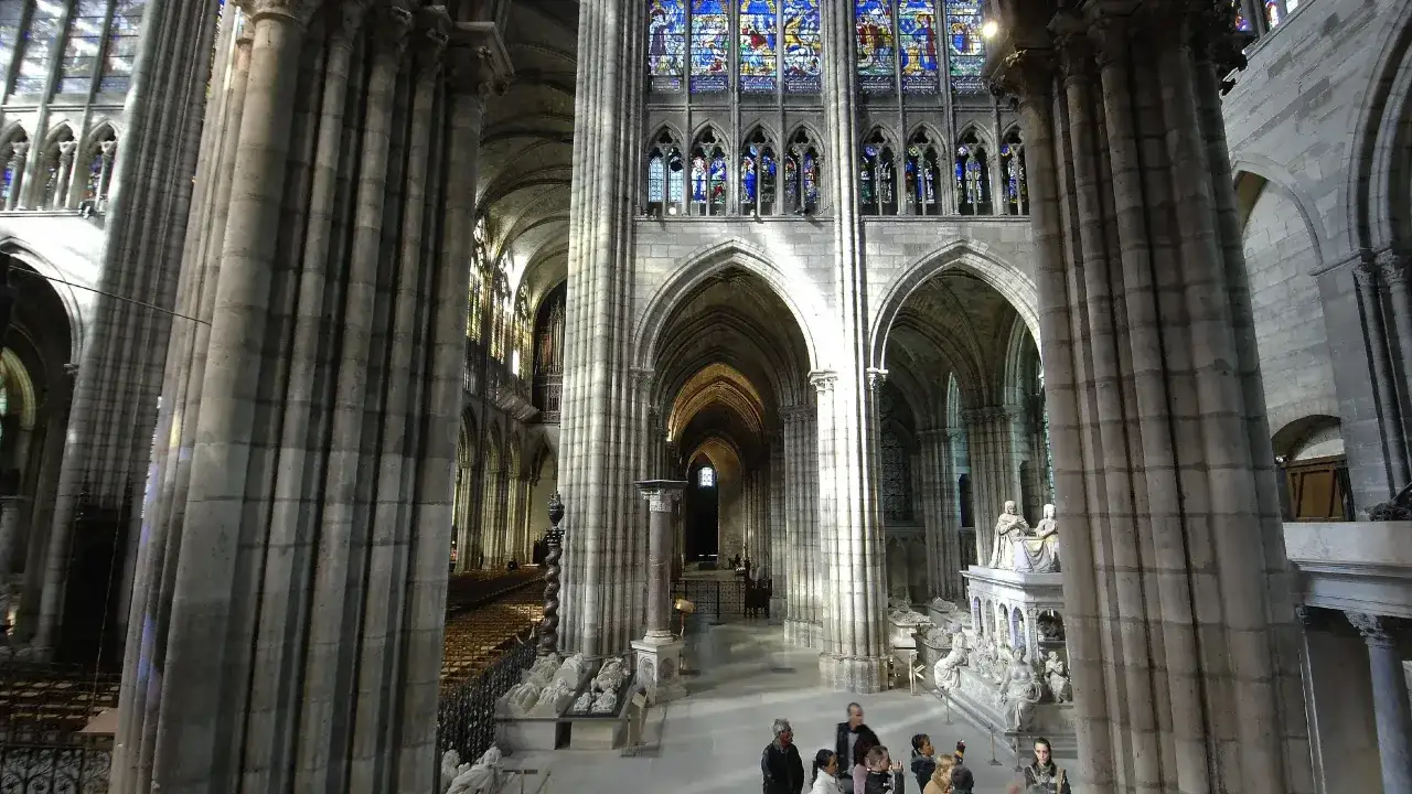 Wnętrze bazyliki Saint-Denis z imponującymi kolumnami, witrażami i nagrobkami.