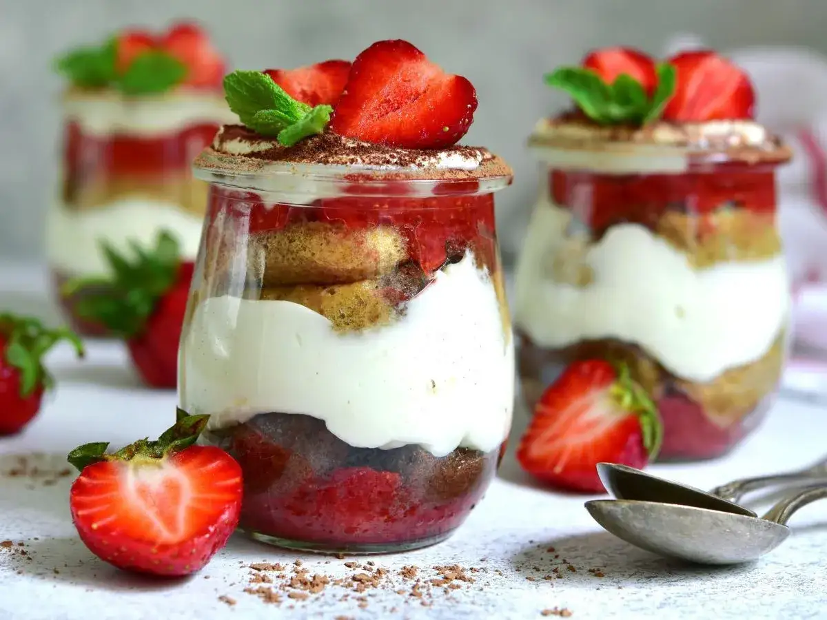 Tiramisu klasyczne kontra tiramisu truskawkowe w słoiczkach. Warstwy biszkoptów, kremu i owoców, ozdobione truskawkami i miętą.