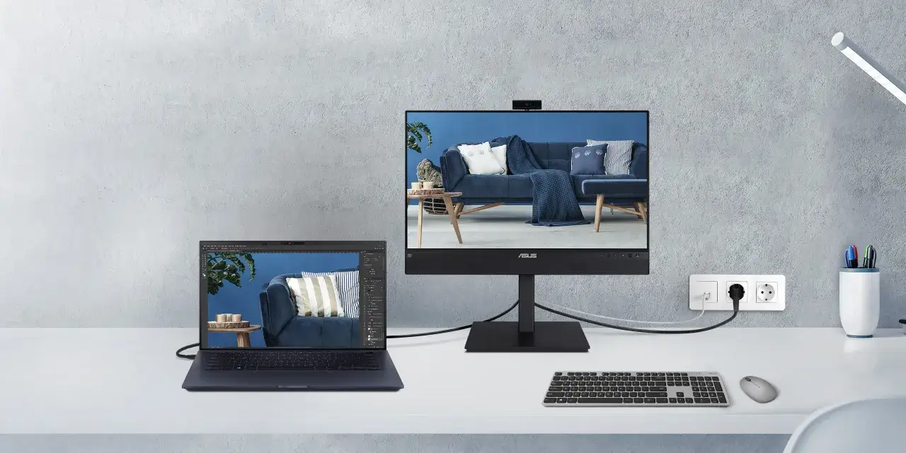 Jak połączyć dwa laptopy? Na biurku stoi otwarty laptop z programem graficznym, obok monitor z obrazem wnętrza.