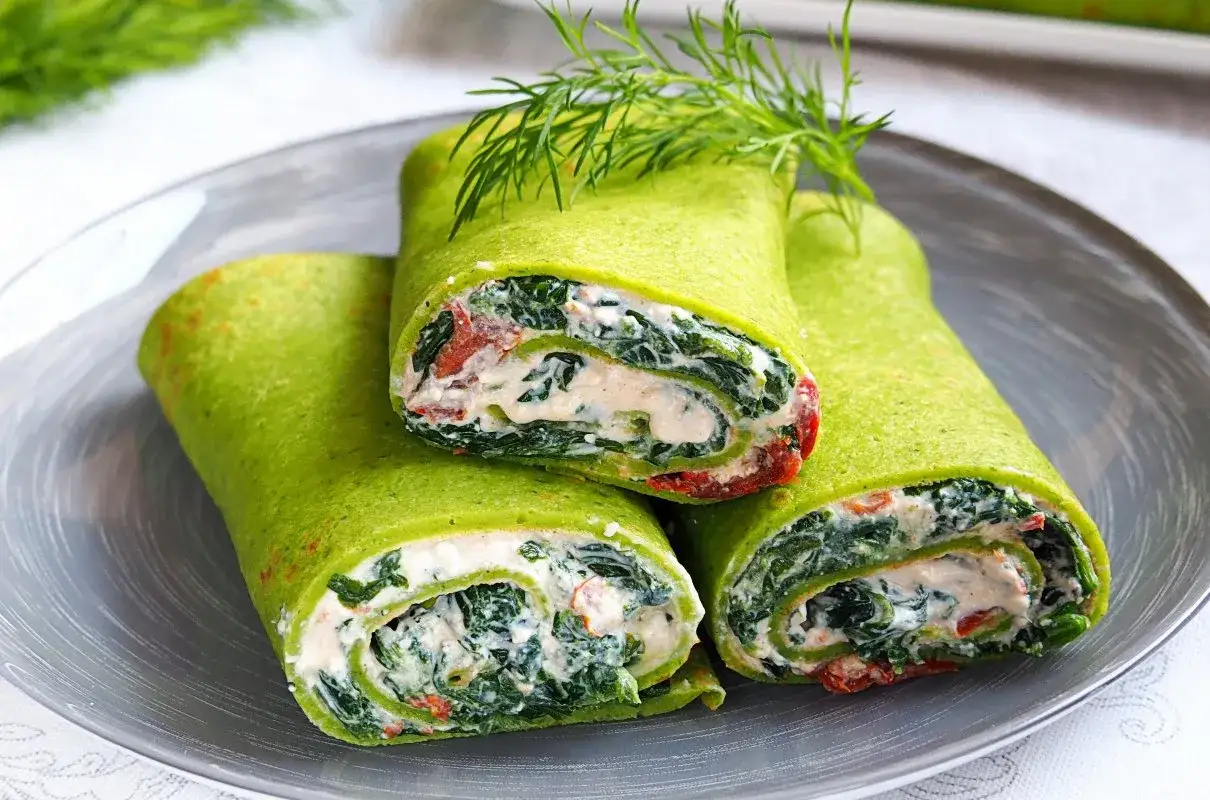 Zielone naleśniki ze szpinakiem mrożonym i kremowym farszem, ozdobione koperkiem. Idealne, gdy zastanawiasz się, jak przyrządzić szpinak mrożony.