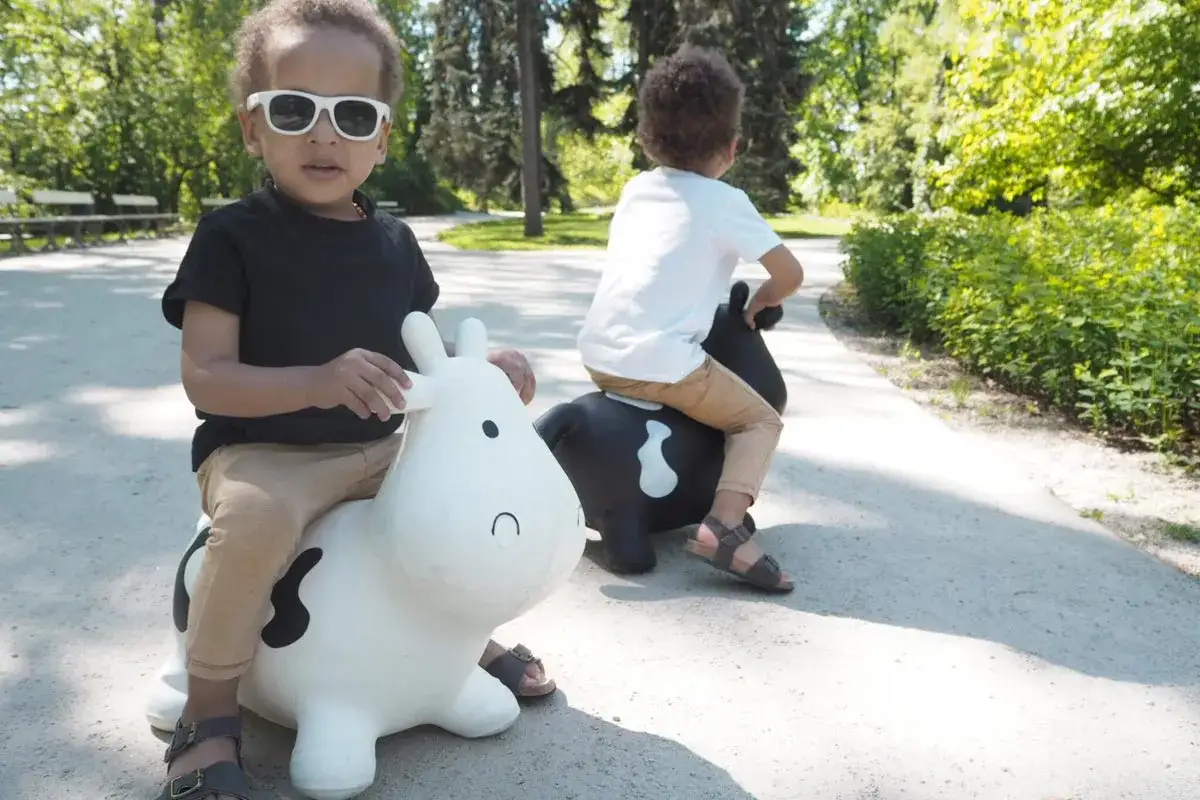 Dzieci wesoło skaczą na dmuchanych krowach. Radosny rozwój 4 latka na świeżym powietrzu.