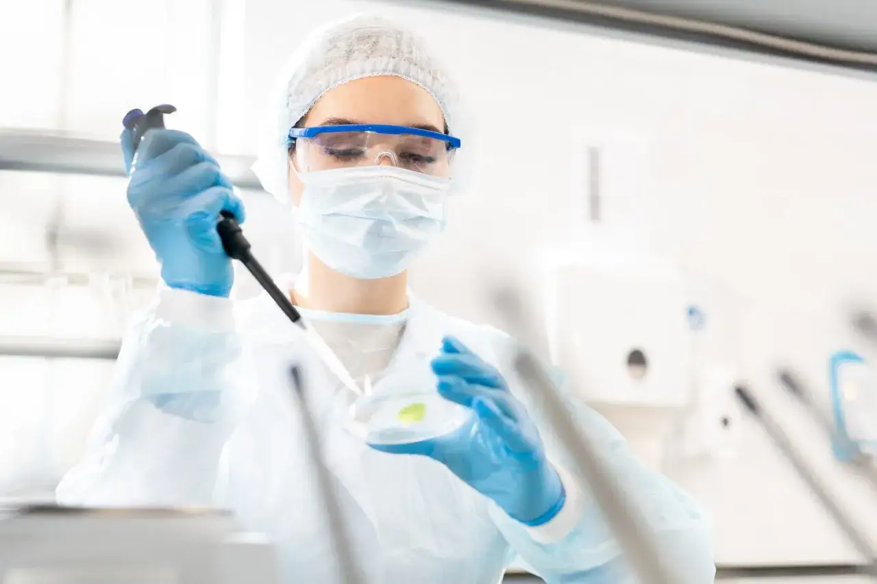 Pracownik laboratorium mikrobiologicznego bada pr&oacute;bkę pod mikroskopem, analizując mikroorganizmy i ich wpływ na środowisko.