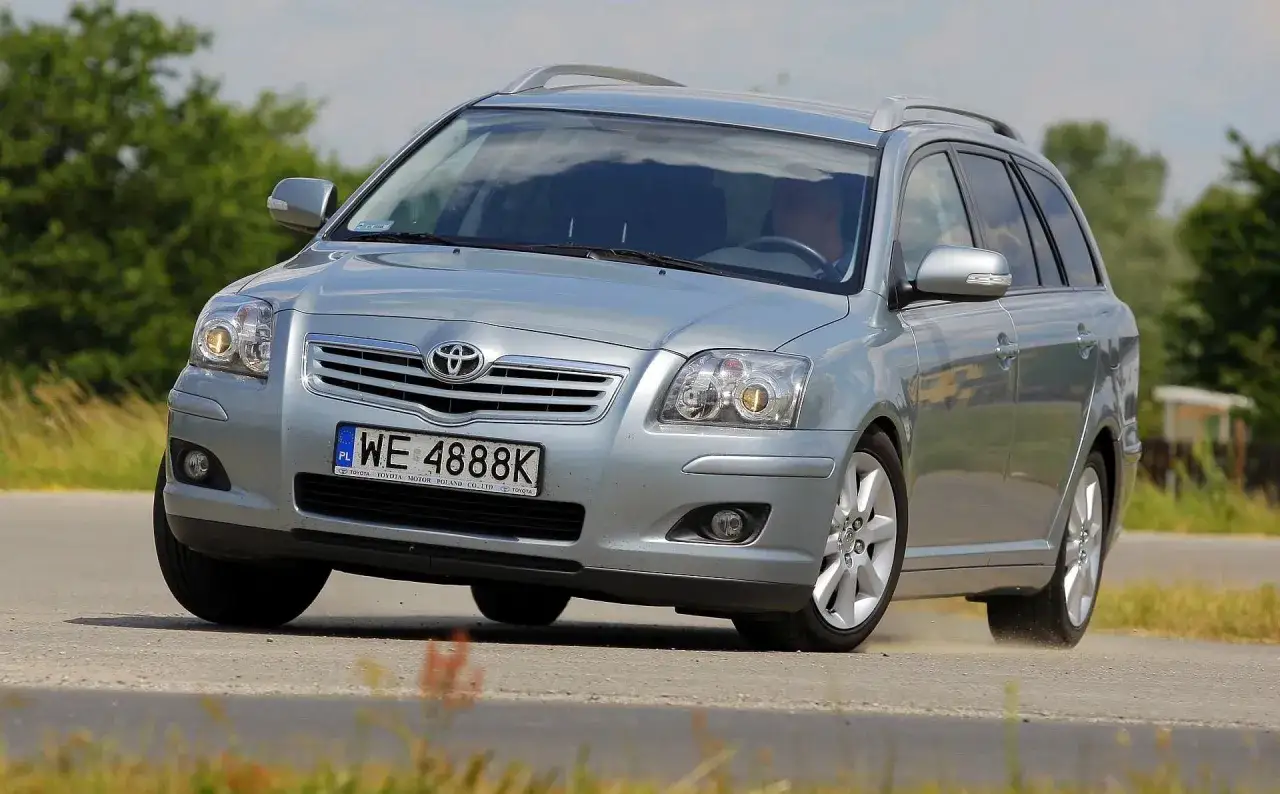 Srebrna Toyota Avensis kombi na zakręcie drogi, z kurzem unoszącym się spod kół.