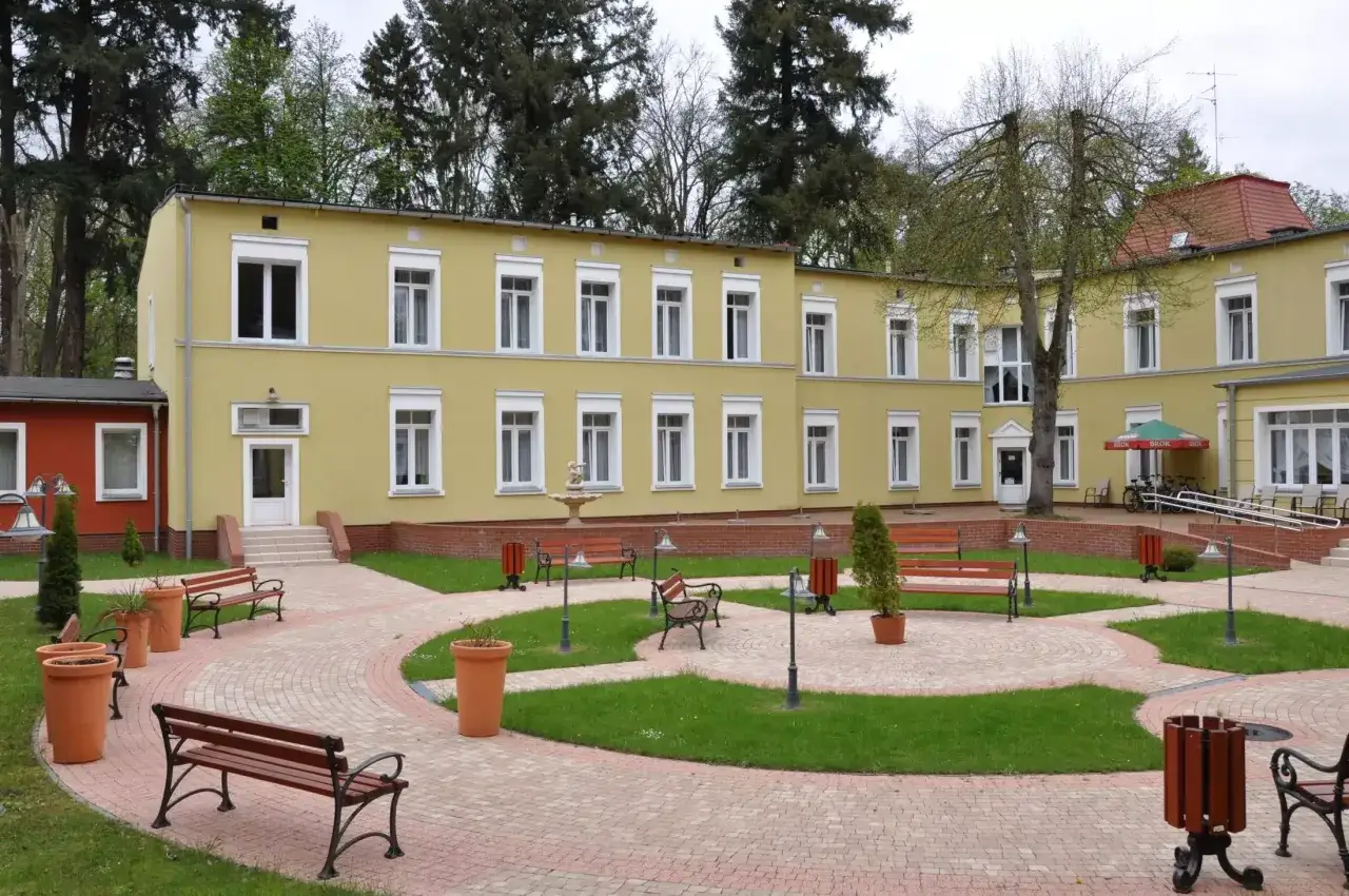 Połczyn-Zdr&oacute;j atrakcje: ż&oacute;łty budynek z oknami, ławki, fontanna i zielony dziedziniec.