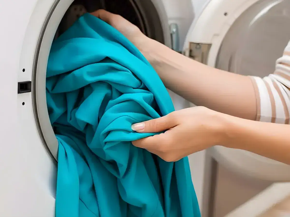 Ręce wkładają turkusową odzież termiczną do pralki. Dowiedz się, jak prać odzież termiczną, by służyła latami.