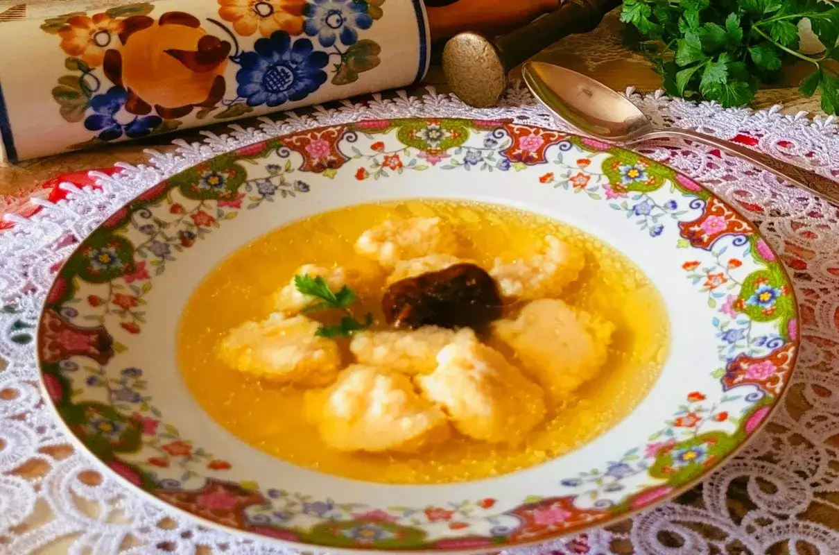 Pyszna zupa z kluskami lanymi, idealna jako inspiracja, co podać na świąteczny obiad. W tle ozdobny wałek i serwetka.