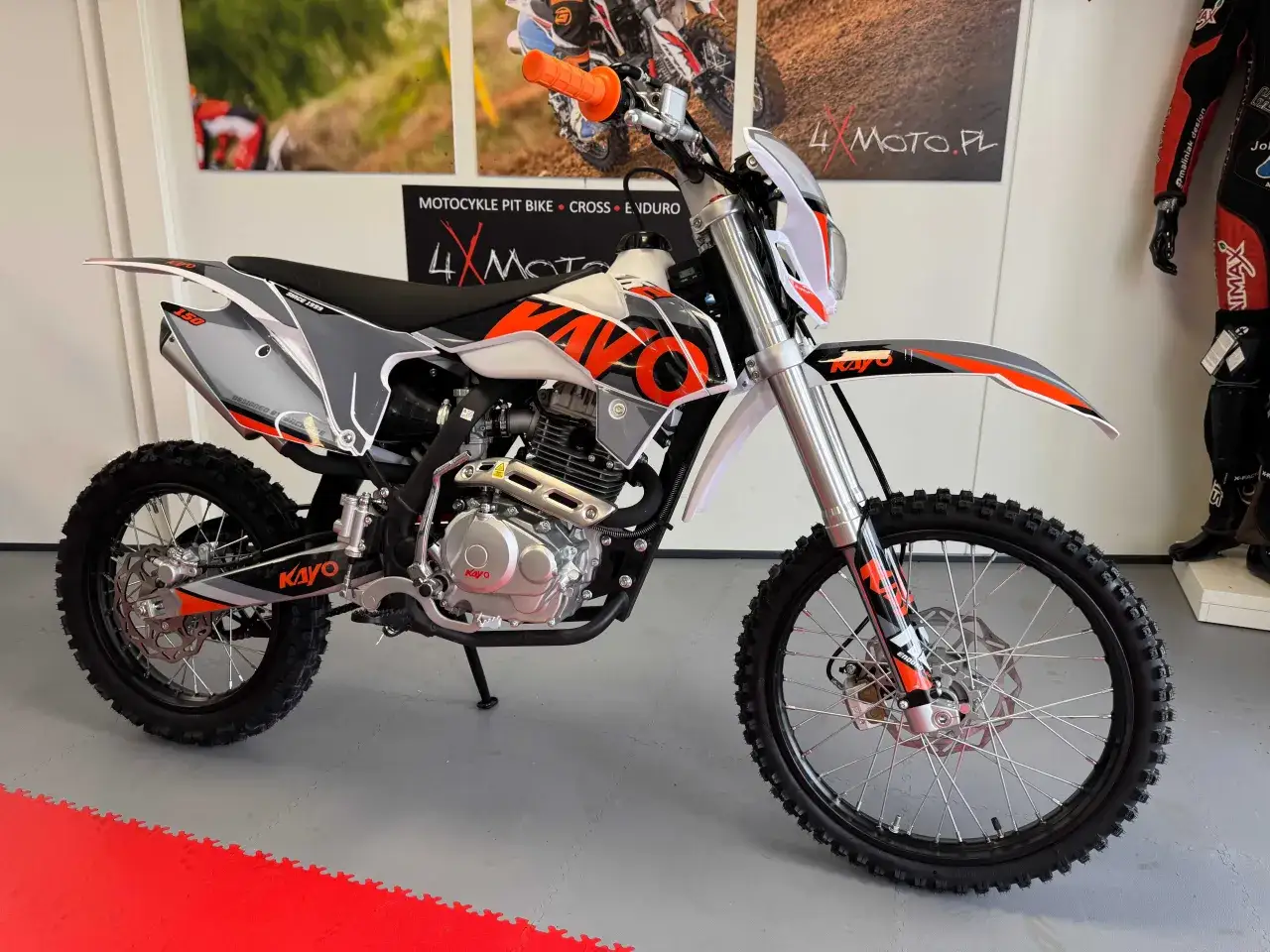 Motocykl Kayo w kolorze białym z pomarańczowymi i szarymi akcentami, gotowy do jazdy po torze cross.