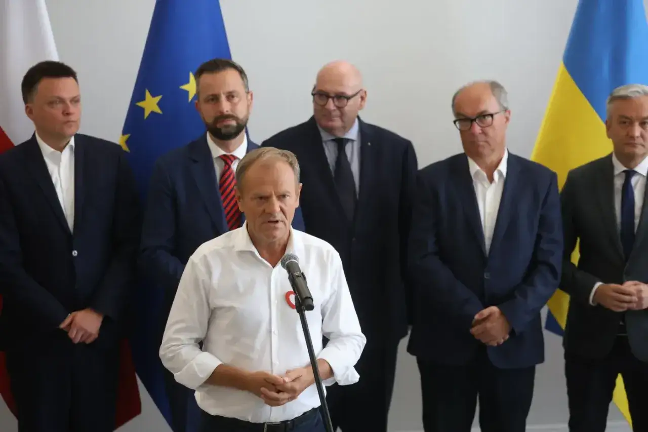 Donald Tusk przemawia podczas konferencji. Za nim stoją politycy na tle flag Polski, UE i Ukrainy. Podpisano umowa koalicyjna tekst.