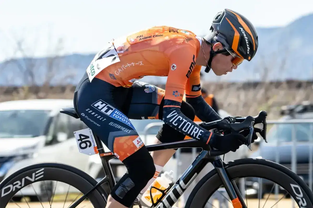 Kolarz w pomarańczowym stroju z numerem 46, pochylony nad kierownicą, walczy o każdy metr. Jego prog mleczanowy jest zapewne wysoki.