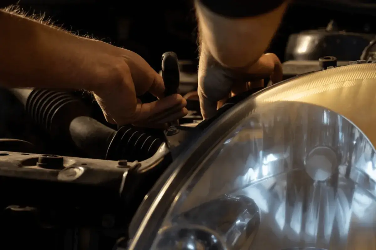 Ręce mechanika samochodowego przykręcają reflektor. Zastanawiasz się, ile zarabia mechanik samochodowy za taką pracę?