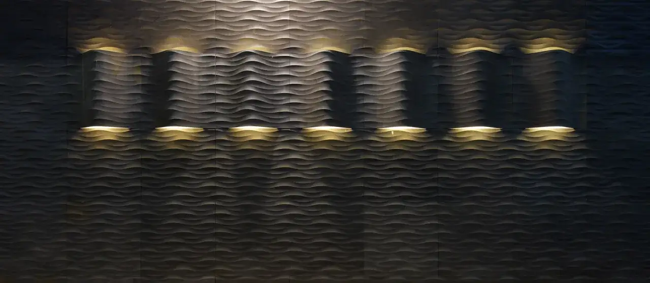 Falista kamienna ściana z subtelnym, ciepłym oświetleniem podkreślającym jej fakturę.