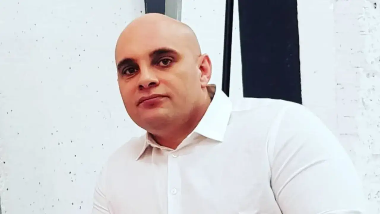 Dominik Abus, wiek nieznany, w białej koszuli na tle białej ściany z czarnym pasem.