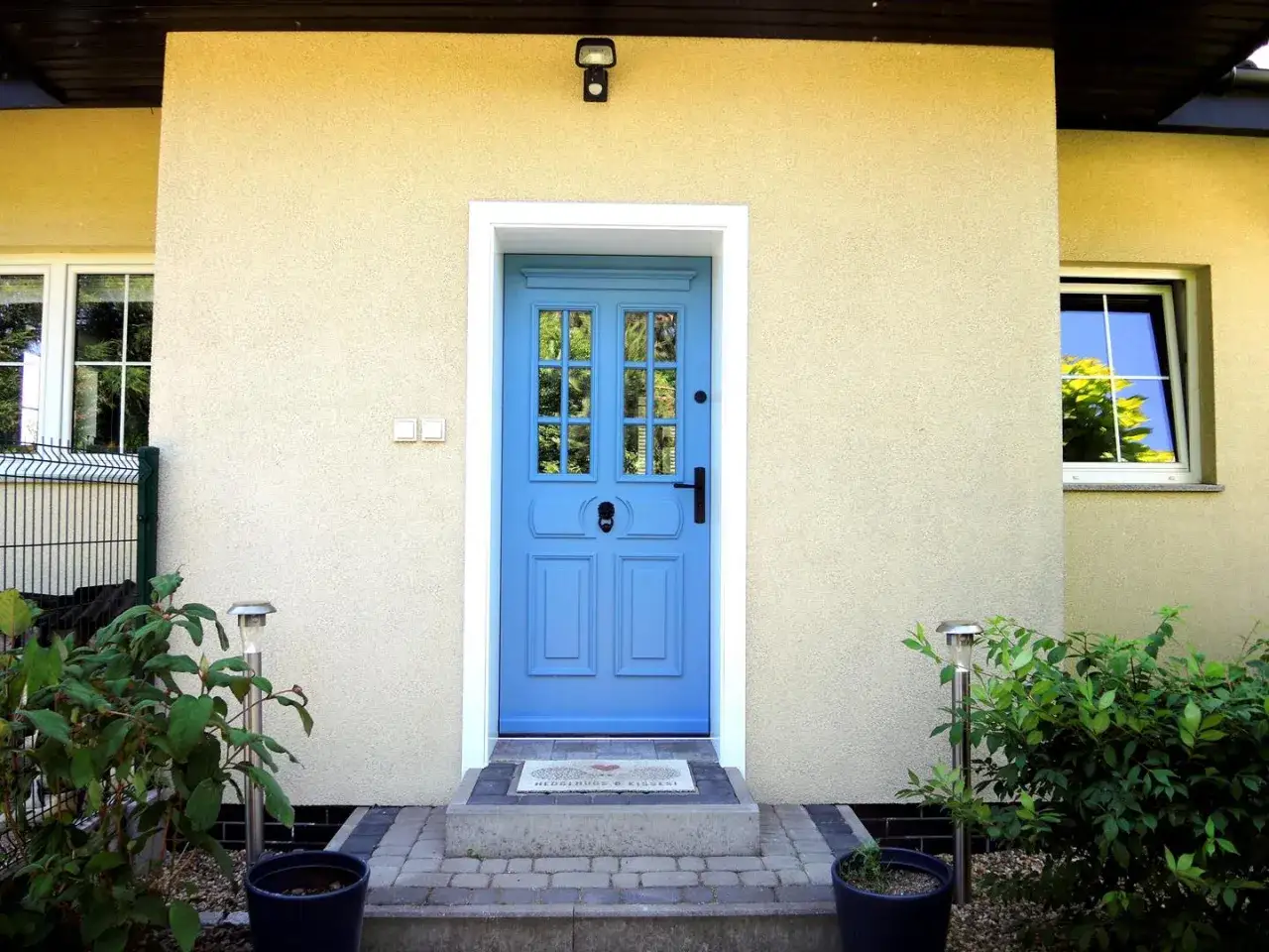 Jasne, oto opis:

Piękne, niebieskie drzwi wejściowe z przeszklonymi panelami prowadzą do przytulnego domu.