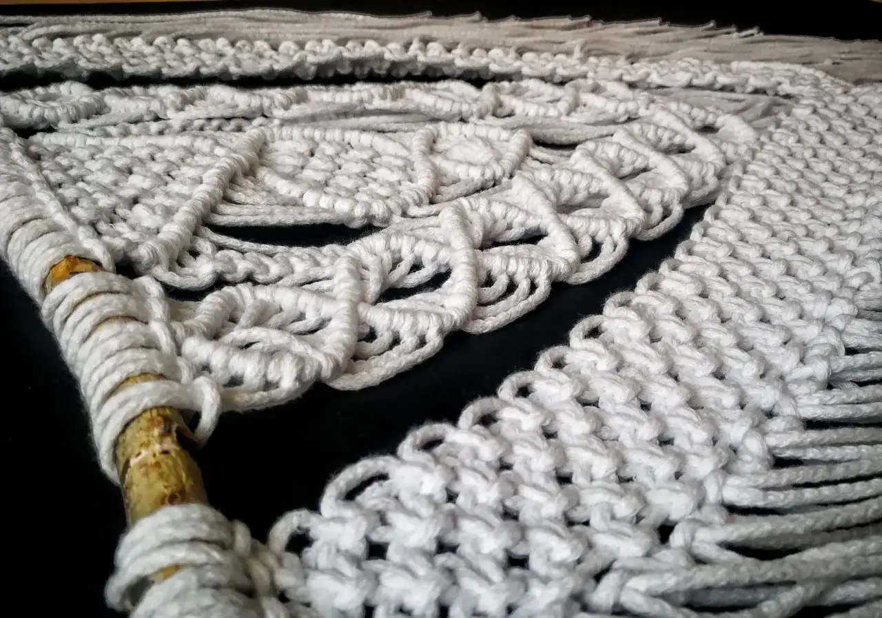 Piękna sztuka plecenia sznurków w makramie. Białe sznurki tworzą misterny wzór na tle czarnego materiału.