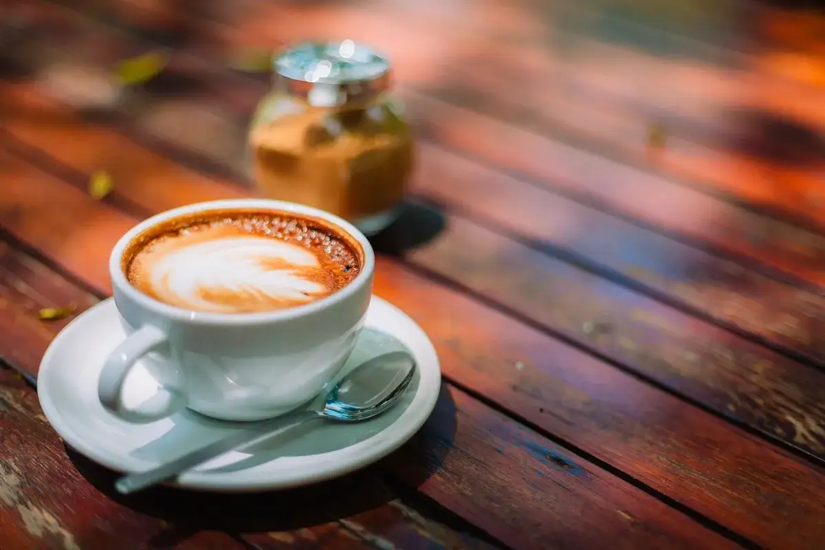 Aromatyczna kawa po włosku z pianką latte art na drewnianym stoliku. Obok słoiczek z cukrem.
