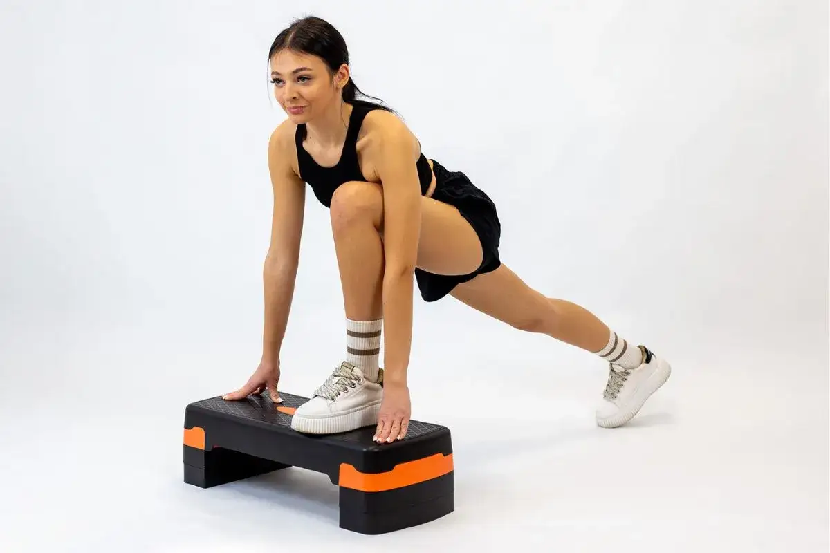 Kobieta w czarnym stroju sportowym wykonuje ćwiczenia na stepperze, rozciągając nogi.