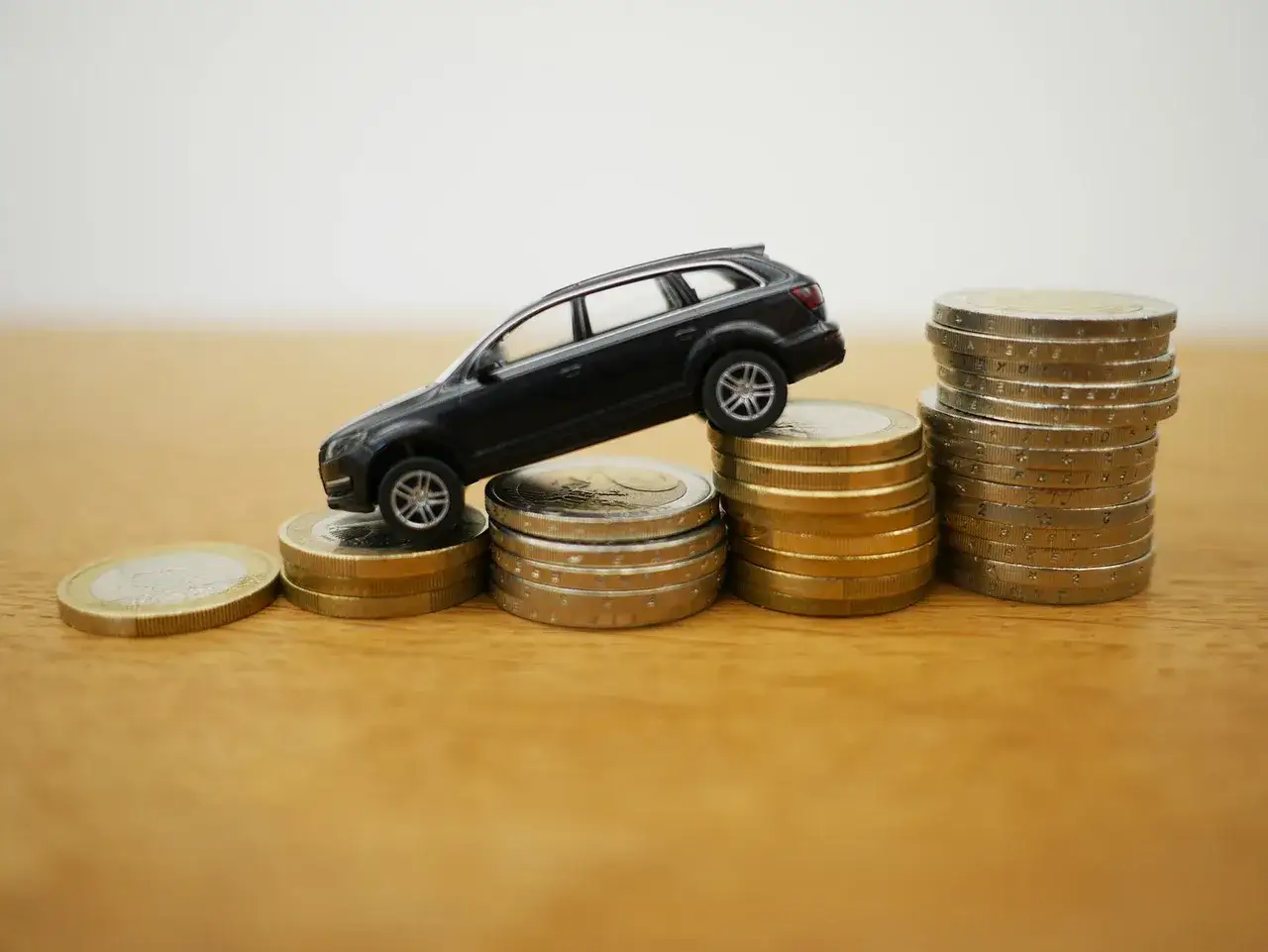 Czarny model samochodu stoi na stosach monet. Dylemat: leasing czy gotówka?