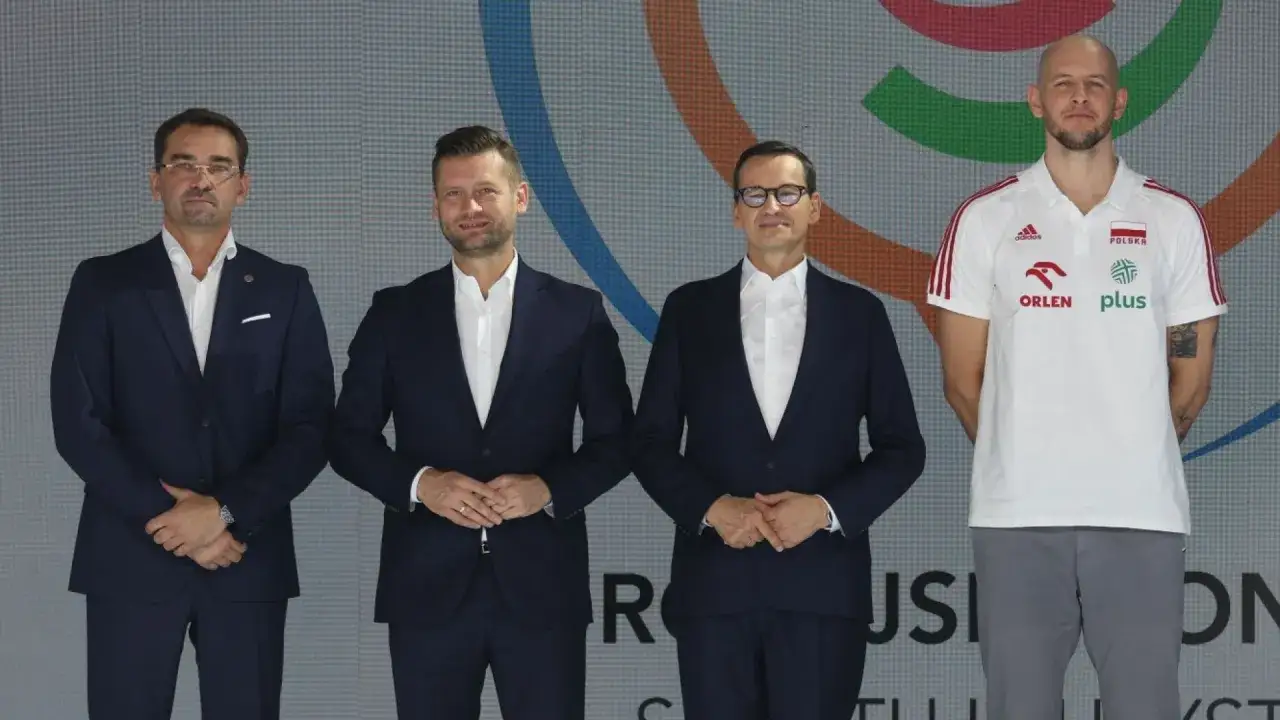 Trzech mężczyzn w garniturach i jeden w koszulce reprezentacji Polski. W tle logo, które może być związane z mistrzostwa świata siatkówka tabela.